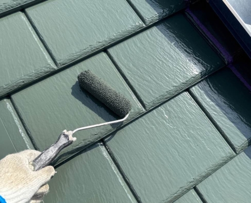 屋根上塗り塗装中の様子。スレート屋根にローラーで主材2回目を均一に塗布している施工風景