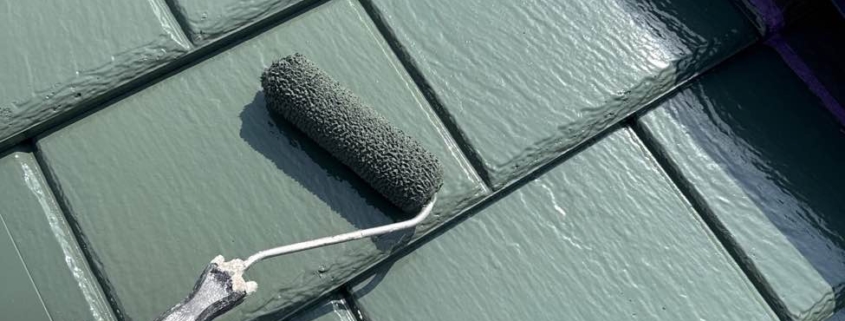 屋根上塗り塗装中の様子。スレート屋根にローラーで主材2回目を均一に塗布している施工風景